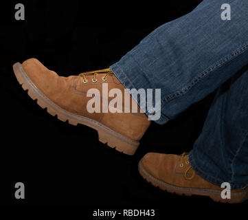 Pair of modern brown suade style boots on mens denim jeans on black background Stock Photo