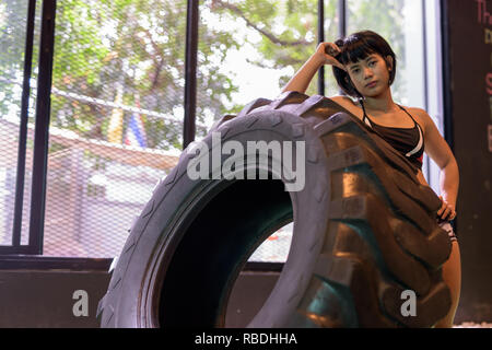 Asian fitness woman pushing and flipping wheel truck tire at gym Stock Photo