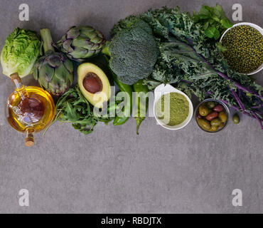 Healthy Green food selection for vegetarians: avocado, apples, broccoli, artichokes, tangerines, mung beans, lettuce, olives, rucola, kale, matcha tea, pears, on gray stone background Stock Photo