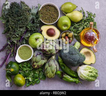 Healthy Green food selection for vegetarians: avocado, apples, broccoli, artichokes, tangerines, mung beans, lettuce, olives, rucola, kale, matcha tea, pears, on gray stone background Stock Photo