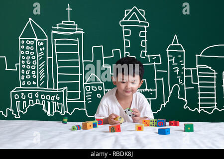Asian kid learning by playing with his imagination about building and engineer architecture drawing and designer, hand drawn on the green chalkboard,  Stock Photo