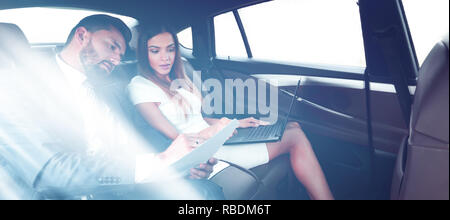 Portrait of two successful business people riding on backseat of taxi: smiling cheerfully and looking at camera on the way to work Stock Photo