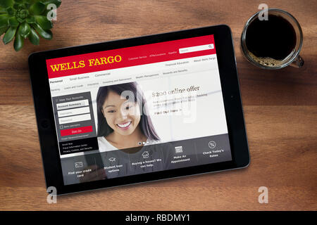 The website of Wells Fargo is seen on an iPad tablet, on a wooden table along with an espresso coffee and a house plant (Editorial use only). Stock Photo