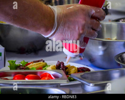 Chef Drizzling a Sauce from a Red Bottle on a Prepared Dish with Stainless Bowls around During Cooking Master Class, Workshop Stock Photo