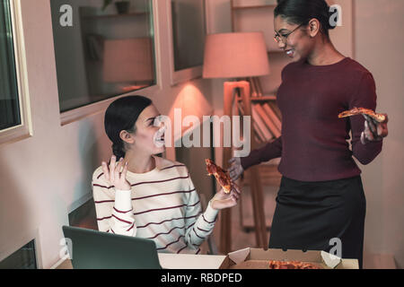 Fast food. Pretty international female keeping smile on her face and standing near her assistant in cabinet Stock Photo