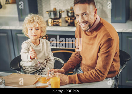 Father and son. Jolly glad man and boy preparing dishes and looking at camera Stock Photo