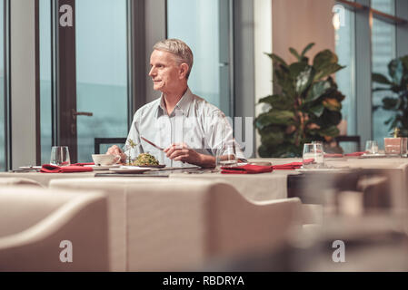 Lunch outside. Pleasant retired man looking through the window while having lunch Stock Photo