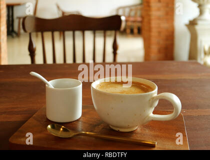 A cup of hot coffee with sugar pot and brass teaspoon served on wooden table in the dining room Stock Photo