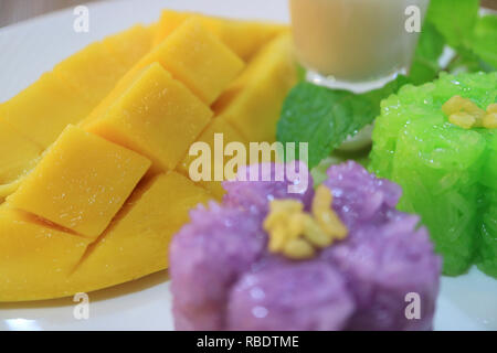 Closed Up Fresh Ripe Mango with Blurry Pea Flowers Sticky Rice in Foreground Stock Photo