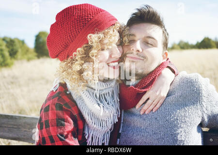 Romantic young couple of a beautiful blonde woman with curly hair and wearing a red wool cap hugs to her boyfriend and a handsome man outdoor Stock Photo