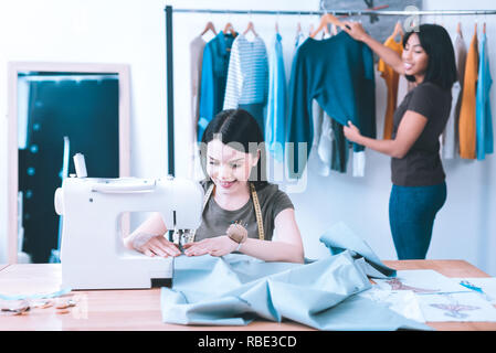 Favorite job. Smiling ingenious girl creating a clothes using sewing machine Stock Photo