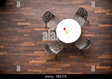 Aerial view of a table and four chairs in a cafeteria. Smoked oak parquet floor. Gerbera in white vase on the table. Copy space to the left. Stock Photo