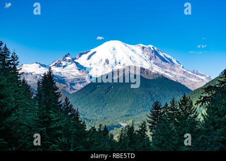 A beautiful view of Mount Rainier on a bright sunny day with the mountain framed by pine trees. Stock Photo