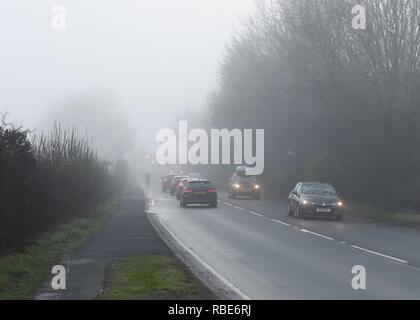 A cyclist with no lights almost disappearing in fog on a busy road near Glasgow in Scotland, UK, Europe. Stock Photo