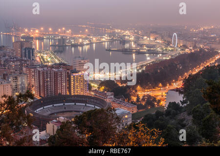 Spanish city of Malaga by night. Harbor and the old town with a bull ring from above in artificial light. Buildings and ships in the harbor can be see Stock Photo