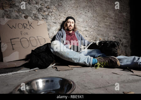 Man in dirty rags hugging dog sitting on sidewalk Stock Photo