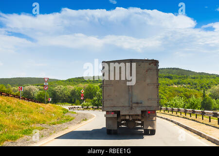 Old truck goes on turning rural road in sunny summer day, rear view Stock Photo