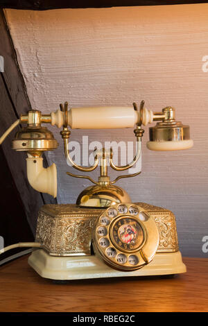 Close-up of antique 1800s ivory and gold rotary dial telephone on top of a dresser in the master bedroom on the upstairs floor inside an old home Stock Photo