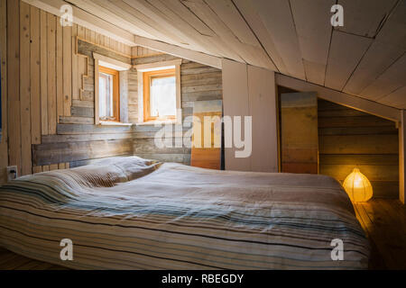 Mezzanine bedroom with old barn wood walls, sloped ceiling and queen size bed on floor inside a rustic 11.5 x 32 foot open concept design mini house Stock Photo