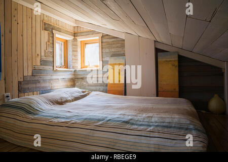 Mezzanine bedroom with old barn wood walls, sloped ceiling and queen size bed on floor inside rustic 11.5 x 32 foot open concept design mini house Stock Photo