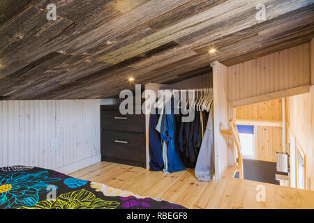 Partial view of upstairs bedroom with queen size bed on pinewood floor and wooden dresser next to clothes closet in mobile mini house Stock Photo