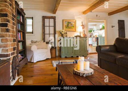 Living room with old wooden grain scale repurposed as coffee table, brown leather sofa and white upholstered sitting chair in old 1862 home Stock Photo