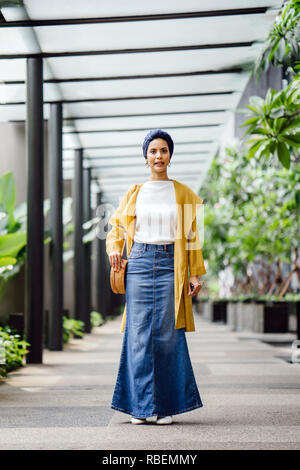 Portrait of a tall, beautiful and elegant Middle Eastern Arab woman in a turban and a pastel outfit standing on a street in the city. Stock Photo