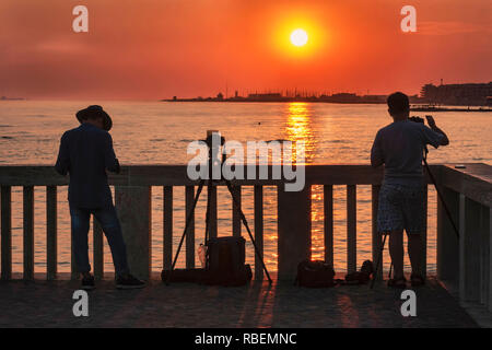 Ostia Lido Rome, Italy - July 26, 2018 :The Roman coast seen from the jetty of Ostia,  Two photographers take a pictures of sunset in its golden hour Stock Photo