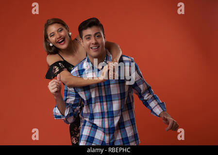 Young happy man carry smiling woman on shoulders isolated on orange color background Stock Photo