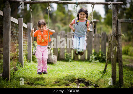 Two young sisters playing on swings in their backyard. Stock Photo