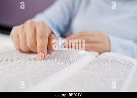 Student in the college library preparing for exams. Learning, gratitude, religion concept. Unrecognizable woman reading big book - Holy Bible and praying. Christian studying scripture. Stock Photo