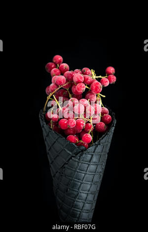 Black wafer cone with frozen redcurrant fruits. Healthy ice cream. Stock Photo