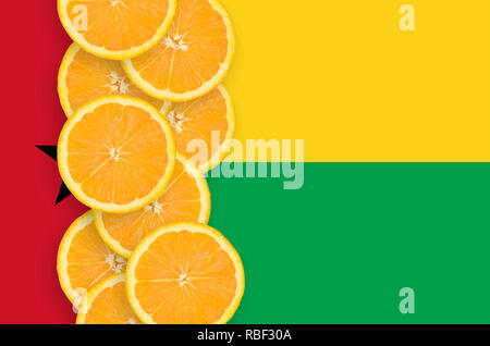 Guinea Bissau flag and vertical row of orange citrus fruit slices. Concept of growing as well as import and export of citrus fruits Stock Photo