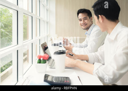 Two Asian businessmen sitting in cafe and discussing business project. Two male employees consulting in cafe. Stock Photo