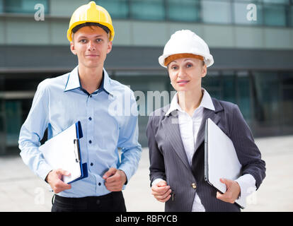 Portrait of smiling architectors who standing with folder and laptop near the building. Stock Photo