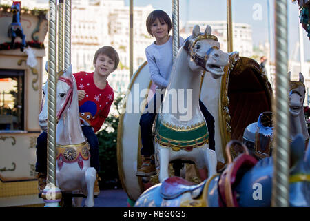 Sweet boys, brothers, riding in a Santa Claus sledge on a merry-go-round, carousel attraction in Europe, active children, wintertime