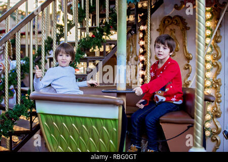 Sweet boys, brothers, riding in a Santa Claus sledge on a merry-go-round, carousel attraction in Europe, active children, wintertime