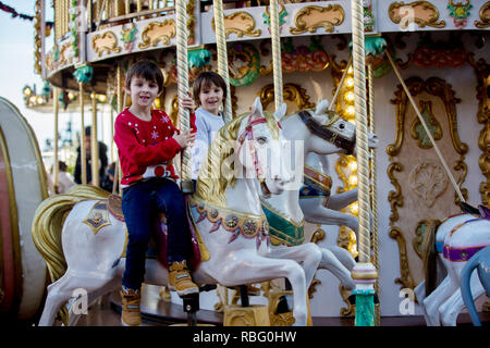 Sweet boys, brothers, riding in a Santa Claus sledge on a merry-go-round, carousel attraction in Europe, active children, wintertime
