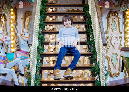Sweet boys, brothers, riding in a Santa Claus sledge on a merry-go-round, carousel attraction in Europe, active children, wintertime