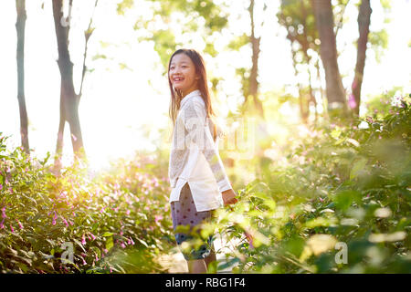 8 year-old beautiful little asian girl standing in flower field looking back and smiling. Stock Photo