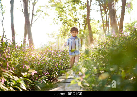 7 year-old cute little asian boy walking through field of flowers in park. Stock Photo