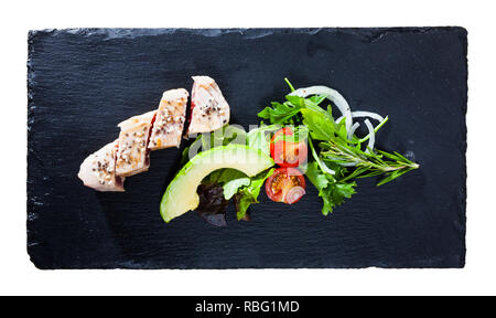Top view of tuna tataki served on black slate board with avocado, fresh tomatoes and greens. Isolated over white background Stock Photo