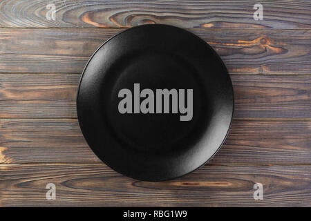 Directy above Empty black matte plate on wooden background. Stock Photo