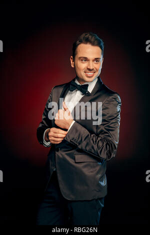 Professional showman wearing suit standing isolated on black and red background looking aside smiling happy Stock Photo