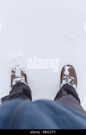 Low section of a person wearing outdoor clothes and shoes and standing on snow in the winter. Copy space. Stock Photo