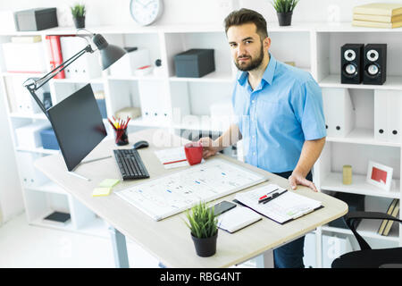 The young man is in the office at the computer table, drinking coffee and working with a magnetic Board. Stock Photo