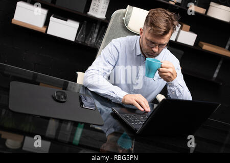 Serious businessman working on laptop and drinking coffee Stock Photo