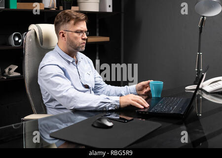 Serious businessman working on laptop and drinking coffee Stock Photo