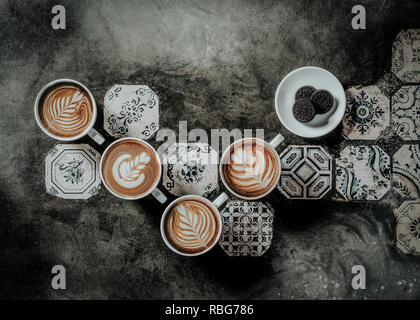 4 cups of coffee taken with natural light , indoor. beautiful latte arts on each cup with a designed floor with hand-made tiles Stock Photo