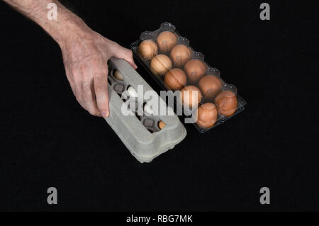 Male hand picking a carton egg box instead of plastic box full of hen eggs on black felt background. Stock Photo